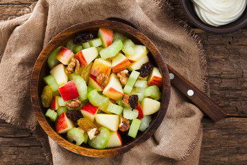 Fresh Waldorf salad made of celery, apple, walnuts, sultanas and raisins in wooden bowl with...
