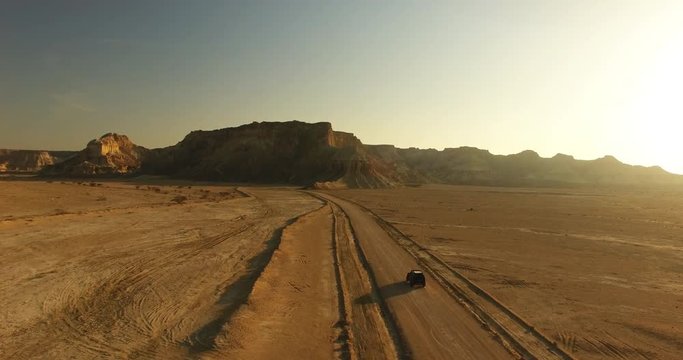 An aerial crane shot of an black offroad car moving middle in great desert 2 An 4WD black offroad car moving along sandy road middle in great desert with mountains during golden hour
