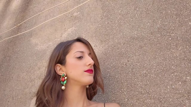Giovane bella ragazza con capelli lunghi, jeans blu e vestito nero sta posando per foto di moda sulla scala all'esterno di casa vicino al terrazzo.