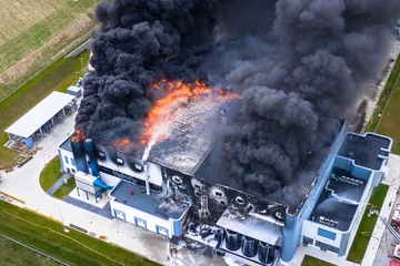 Gordijnen Luchtfoto van verbrand industrieel magazijn of logistiek centrumgebouw na grote brand met enorme rook van verbrand dak © Lukasz Janyst