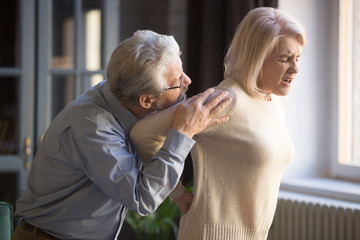 Mature woman suffering from sudden backache, old man supporting her