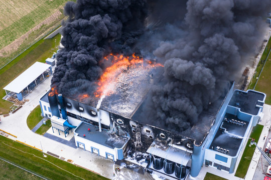 Aerial view of burnt industrial warehouse or logistics center building after big fire with huge smoke from burned roof
