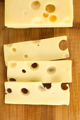 Emmentaler Käse am Stück und in Scheiben auf Holzbrett (Selektiver Fokus, Fokus auf die Käsescheiben)