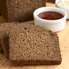 Slices of pumpernickel dark rye bread on cutting board with jam and cream cheese, photographed with...