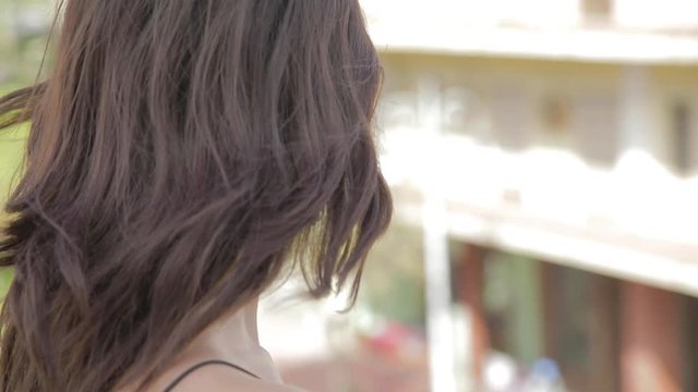 Bellissima ragazza con capelli lisci maglia nera, jeans blu e orecchini affacciata dal terrazzo di casa.