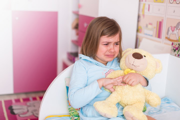 Cute adorable little girl crying in children's room hugging teddy bear. Childhood, sadness concept