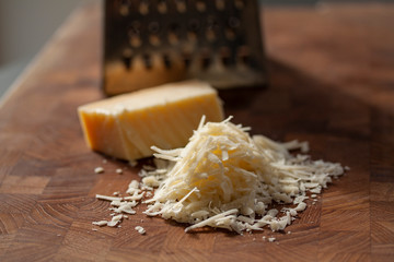 Grated italian parmesan cheese on wooden chopping board with a block of parmasan and a grater in...