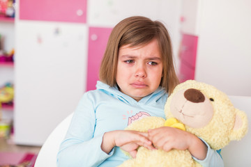 Cute adorable little girl crying in children's room hugging teddy bear. Childhood, sadness concept