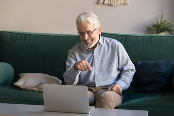 Smiling grey haired mature man using laptop, making video call