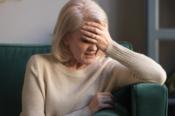 Unhappy mature grey haired woman suffering from headache close up