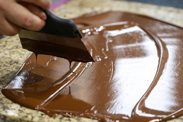 Chocolatier with a spatula is stirring the tempered liquid chocolate on a granite table
