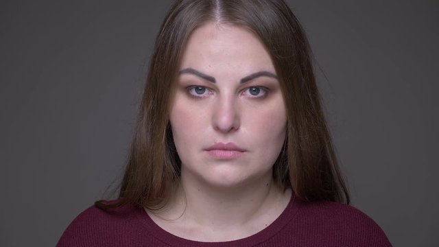 Closeup portarit of young overweight caucasian female with brunette hair looking at camera with background isolated on gray