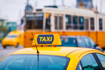 Yellow taxi cab with blurred tram and cars in the background