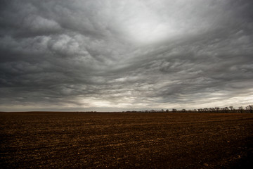 huge, blue clouds slowly float across the sky, over just plowed field, early spring morning