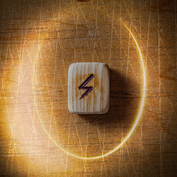 Sowilo. Handmade scandinavian wooden runes on a wooden vintage background in a circle of light. Concept of fortune telling and prediction of the future.