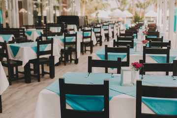 Abstract blur interior of a modern resort restaurant with blue tablecloths for background. Wooden floor, cozy vacation atmosphere, sunny summer day.