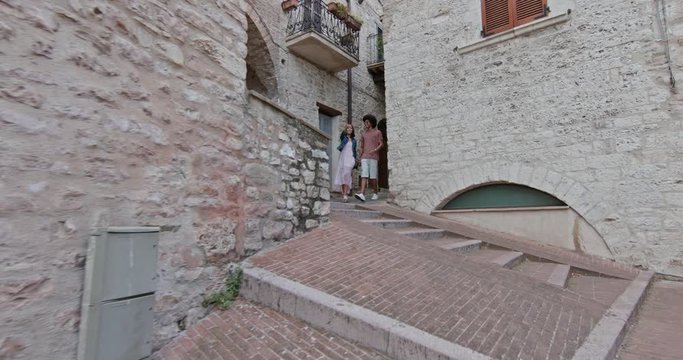 Romantic couple walking visiting rural town of Assisi.Side follow. Friends italian trip in Umbria.4k slow motion