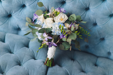 A beautiful multicolored wedding bouquet with wildflowers and roses lies against the blue sofa. Wedding photography, copy space, poster.