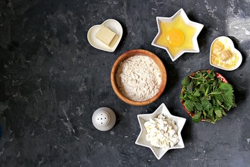 Ingredients for cooking gnocchi or dumplings with nettle on a dark gray concrete background: ricotta cheese, fresh nettle, egg, wheat flour, parmesan cheese, butter, salt. Top view, copy space.