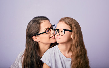 Happy young casual mother and smiling kid in fashion glasses hugging and looking each other on purple background with empty copy space.