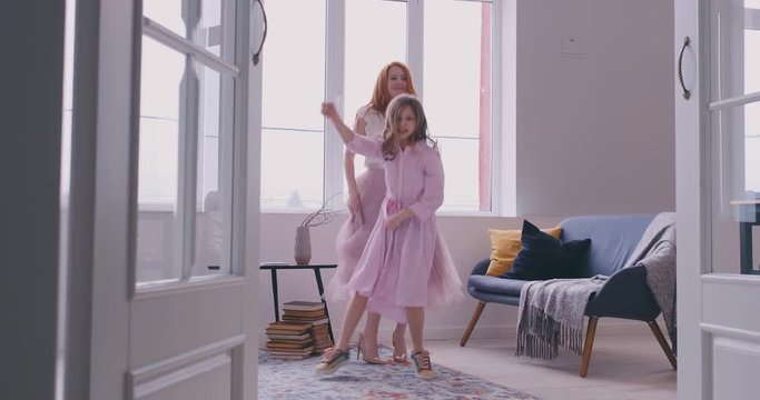 Active young mom babysiter and cute little kid daughter jumping dancing in modern house living room, happy family mother with child girl having fun enjoy playing funny activity together at home