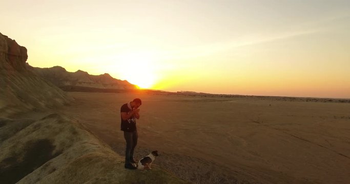 A rotating aerial shot of a man and his dog playing harmonica during sunset 2 An aerial shot of a man and his puppy standing on top of a hill  and playing harmonica long shadows golden hour