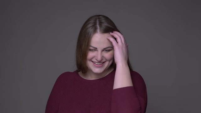 Closeup portarit of young cute overweight caucasian female smiling with shyness looking at camera with background isolated on gray