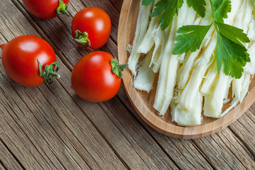 string cheese in bamboo bowl with cherry tomatoes on wooden background. Cecil or chivil cheese, turkish food breakfast cheese concept