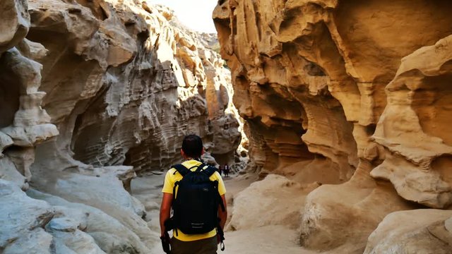 A following shot of tourist man walks into an incredible canyon   2 A yellow color wearing tourist man walks along to a wonderful canyon natural sun light through the canyon
