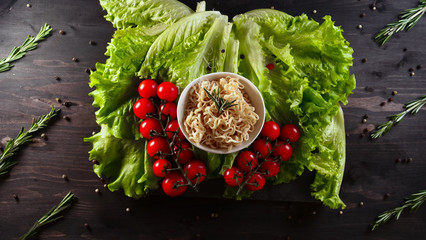 Background of lettuce leaves and a wooden table, a ready-made dish of vegetable noodles and a sea of products are being detained and then tried (eaten) with Chinese sticks. Concept: Shrimps, Vegetable
