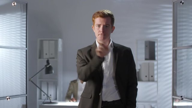 Young caucasian businessman in formal suit tapping and swiping on invisible augmented reality display while working in office. Footage suitable for adding AR graphics