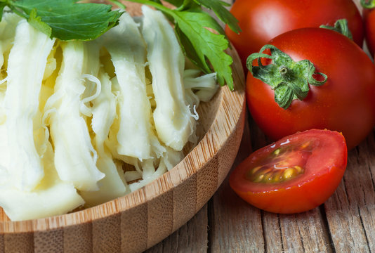 string cheese in bamboo bowl with cherry tomatoes on wooden background. Cecil or chivil cheese, turkish food breakfast cheese concept