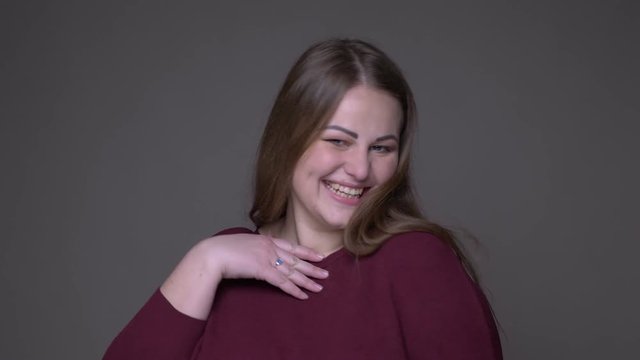 Closeup portarit of young overweight caucasian female smiling and waving hi with a hand with background isolated on gray