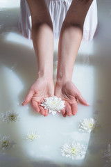 Obraz na płótnie Canvas photo white flower in female hands in a natural milk bath with foam and flowers