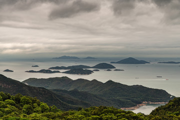 Obraz premium Hong Kong, China - March 7, 2019: Lantau Island. Pearl River estuary and South China Sea seen from Tian Tan Buddha platform. Green forested hill up front. Islands, boats, shorelines under heavy rainy 