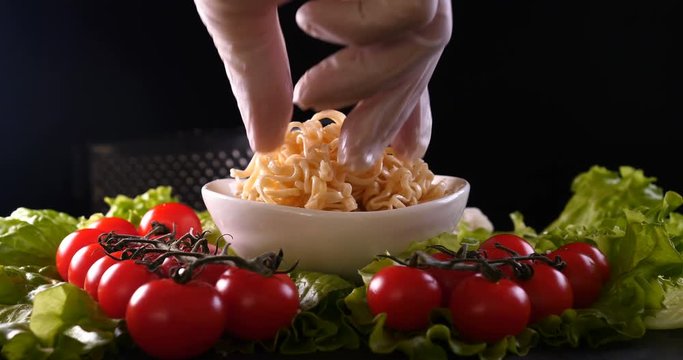 On a black background, vegetables and noodles on a wooden table, the whole dish is rubbed on top with parmesan cheese and mixed noodles. Concept of: Grater, Cheese, Noodles, Cherie Tomatoes, Salad.