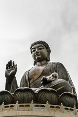 Hong Kong, China - March 7, 2019: Lantau Island. Frontal view of Tian Tan Buddha statue from down under showing face, chest, lotus leaves and stone fence under silver sky.