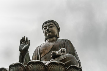 Hong Kong, China - March 7, 2019: Lantau Island. Frontal Closeup of Tian Tan Buddha statue from down under showing face, chest and lotus leaf under silver sky.