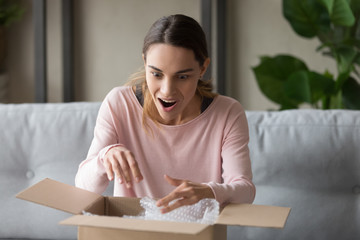 Surprised woman unpacks carton box at home feels happy