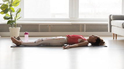 Woman side view lying on yoga mat practicing corpse pose