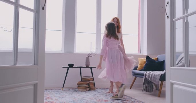 Active young mom babysiter and cute little kid daughter jumping dancing in modern house living room, happy family mother with child girl having fun enjoy playing funny activity together at home