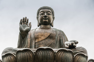 Hong Kong, China - March 7, 2019: Lantau Island. Frontal Facial closeup of Tian Tan Buddha statue from down under showing face, chest, and lotus leaves under silver sky.