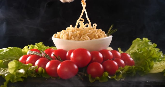 On a black background, vegetables and noodles on a wooden table, the whole dish is rubbed on top with parmesan cheese and mixed noodles. Concept of: Grater, Cheese, Noodles, Cherie Tomatoes, Salad.