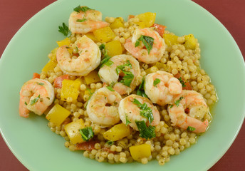 Shrimp, yellow bell peppers and pearl couscous dinner on green plate on red table