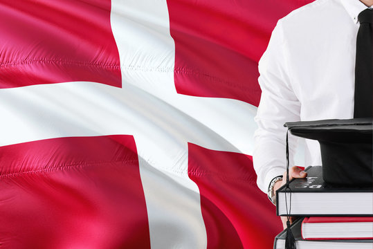 Successful Danish Student Education Concept. Holding Books And Graduation Cap Over Denmark Flag Background.