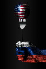 A hand with a drawn Russia flag holds a fork, on which is a ball with a drawn USA flag, a sign of...