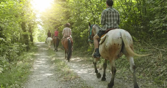 Four active people riding horses on a sunny outdoor wild forest field.Friends italian trip in Umbria.4k slow motion