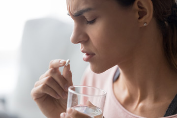 Closeup of frown woman holding pill and glass of water