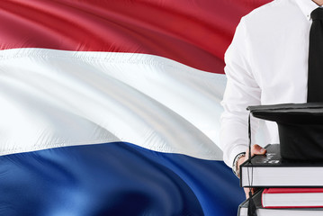 Successful Dutch student education concept. Holding books and graduation cap over Netherlands flag background.
