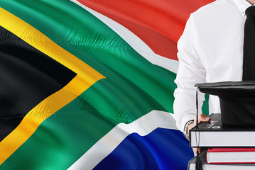 Successful student education concept. Holding books and graduation cap over South Africa flag...